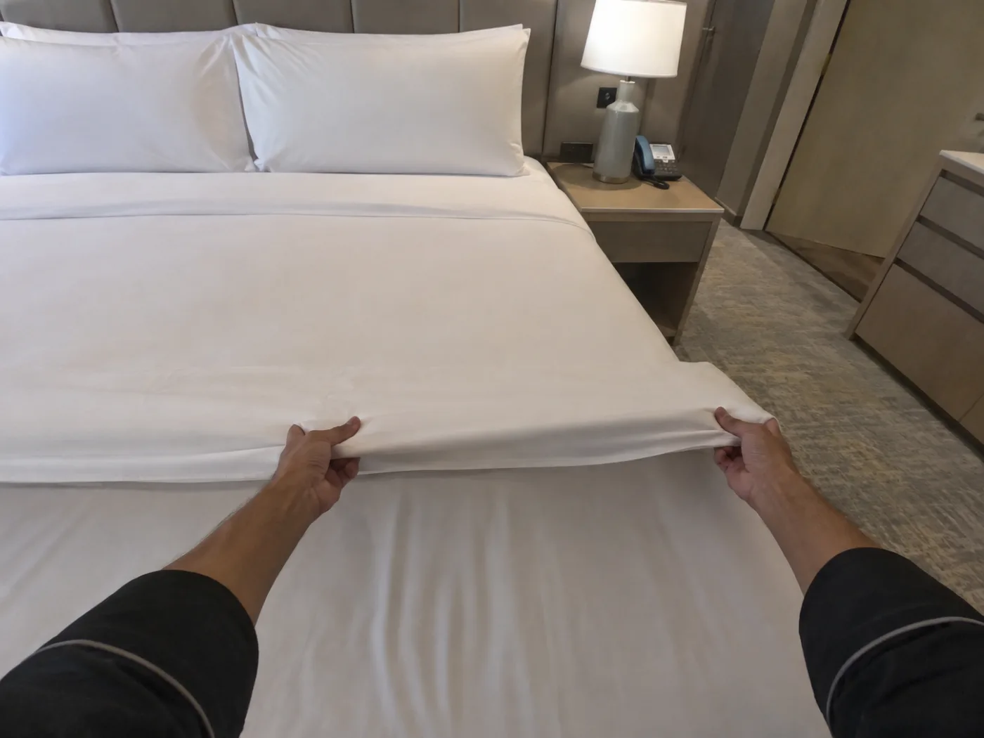 First-person view down at hands drawing a sheet across a bed in a hotel room. No faces in frame.